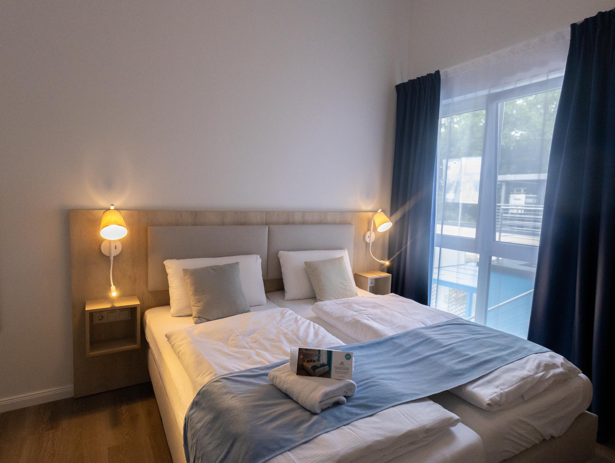 Admiralzimmer – Doppelbett mit Holzkopfteil, Leselampen und Fenster zum Balkon